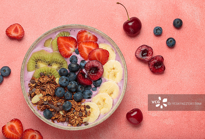 高角度拍摄的鲜艳冰沙碗，配有新鲜水果和格兰诺拉麦片，背景为粉色图片素材
