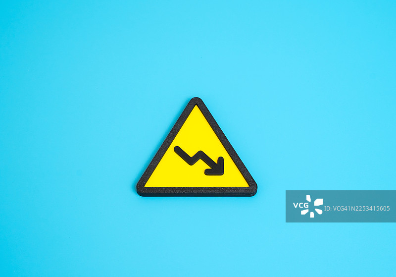 蓝色背景上的黄色警告标志，带有向下的趋势箭头，象征着金融危机或衰退图片素材
