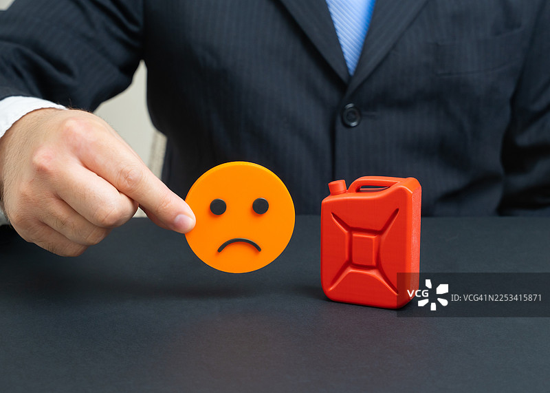 一位商务人士指向一个红色的汽油罐旁边的悲伤表情符号，象征着高昂的燃油价格和经济困境图片素材