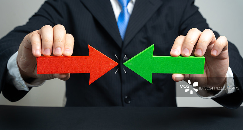 身着西装的商人手持红绿箭头，指向彼此，象征冲突或相反的方向图片素材