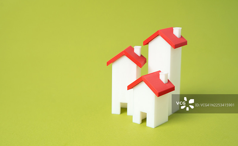 在充满活力的绿色背景上，有三栋带有红色屋顶和白色墙壁的微型模型房屋，代表房地产和住房概念图片素材