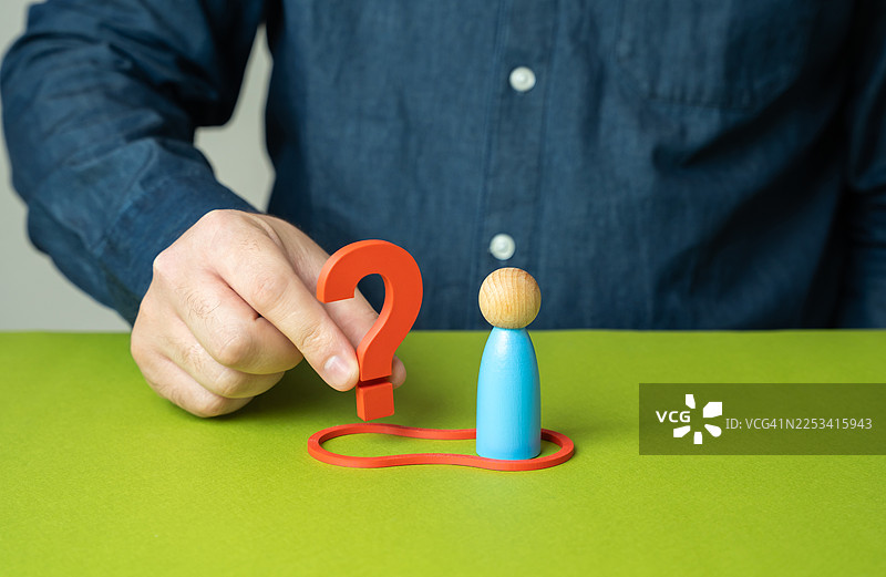 商人的手将一个红色的问号放在绿色桌子上的木偶旁边，象征着解决问题或不确定性图片素材