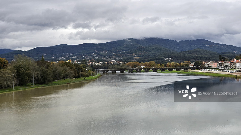 葡萄牙，蓬特德利马，一座古老的石桥、城镇和群山在多云天空下的风景优美的河流景色图片素材