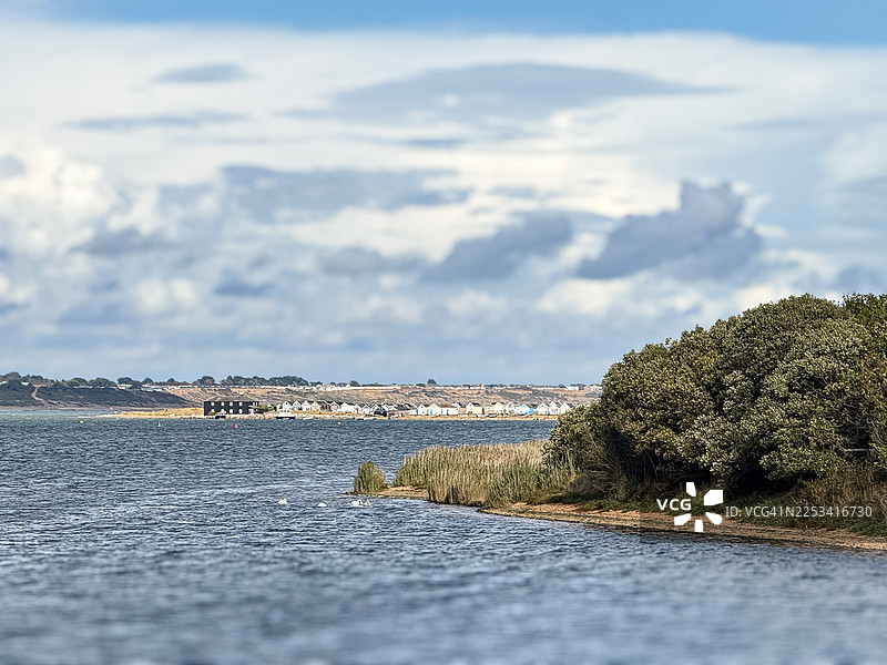 英国南伯恩，多云天气下，宁静的海景，远处的房屋和郁郁葱葱的绿色海岸线图片素材