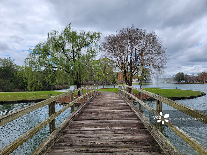宁静公园景致中，绿树成荫，天空多云，一座木制人行桥横跨水面图片素材