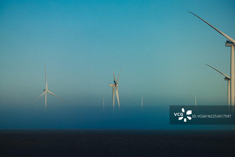 在晴朗蓝天下，风力发电机从薄雾笼罩的田野中升起，象征着清洁能源和可持续的未来，美国，德克萨斯州，科珀斯克里斯蒂图片素材
