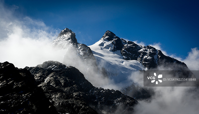 乌干达，白雪皑皑的雄伟山脉笼罩在云雾中，背景是晴朗的蓝天图片素材