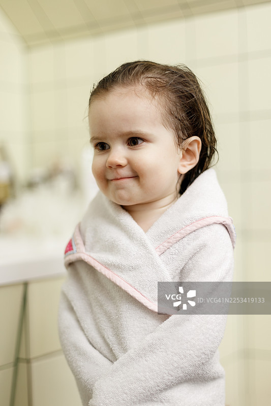 洗完澡后，可爱的小孩裹着白色毛巾，头发湿漉漉地在浴室里笑着。图片素材