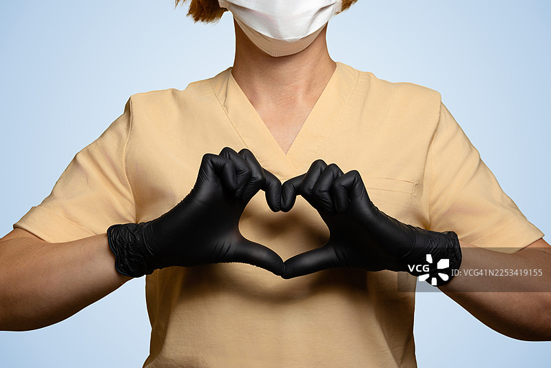 身穿防护服、戴着口罩的医护人员用戴着手套的双手比出爱心形状，象征着关怀与感恩图片素材