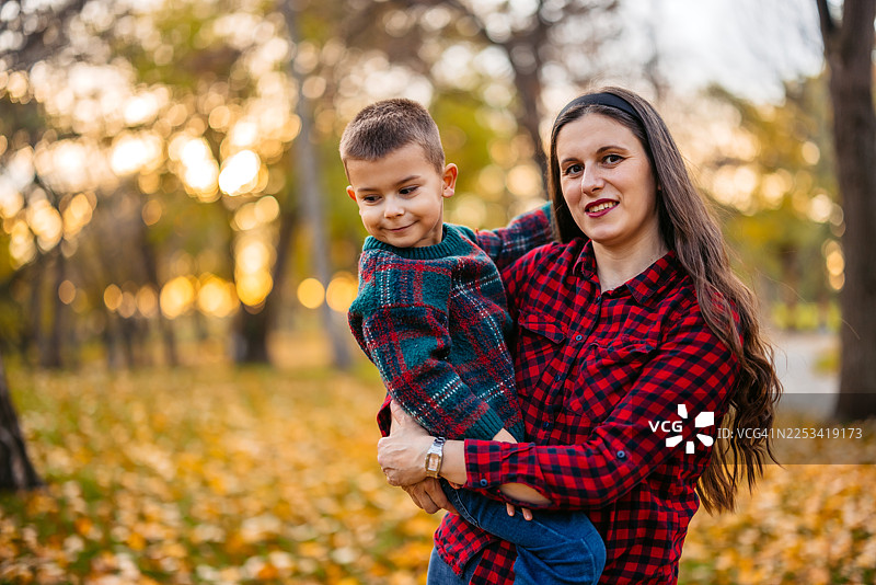 秋日，年轻的母亲在公园里抱着她学龄前的儿子图片素材