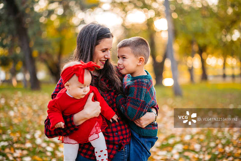 秋季在公园里，一位年轻的母亲带着她学龄前的小儿子和婴儿女儿图片素材