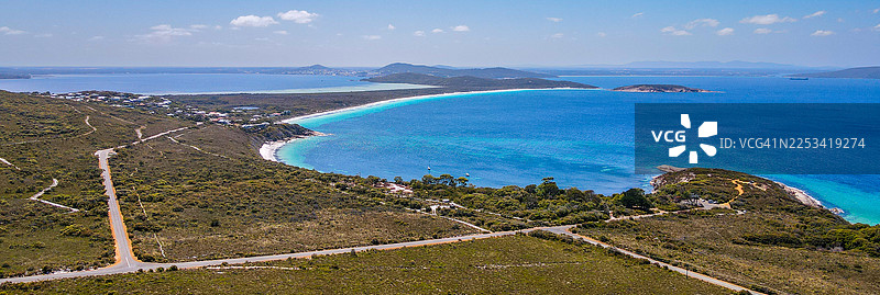 从高处全景俯瞰，碧绿的海水和白色沙滩勾勒出迷人的海湾，四周环绕着苍翠的山丘，天空湛蓝清澈。图片素材