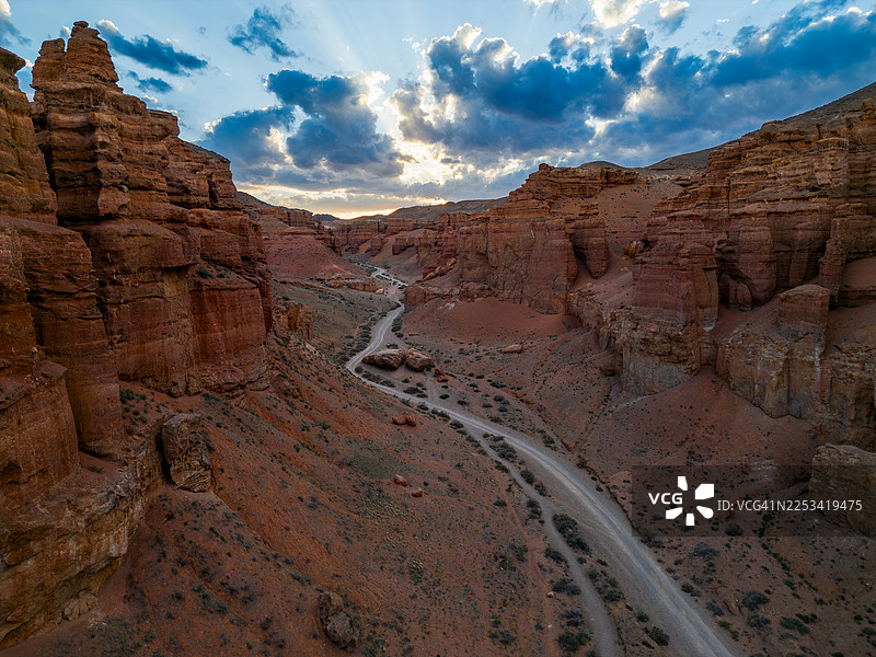 夕阳下，哈萨克斯坦一处荒漠峡谷的戏剧性景观，一条蜿蜒的公路在多云的天空下延伸图片素材