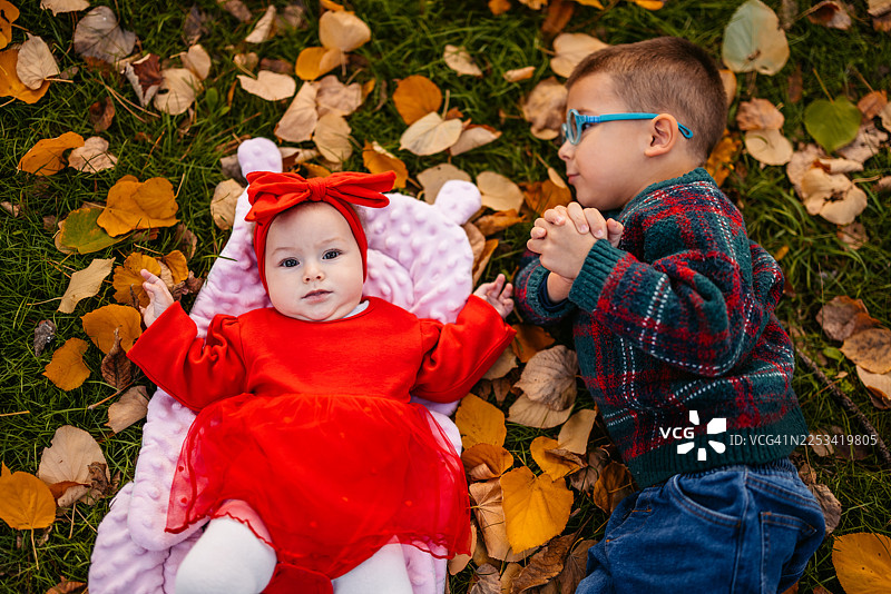 一个学龄前男孩和他的小妹妹在秋季的公园里，躺在落叶上图片素材