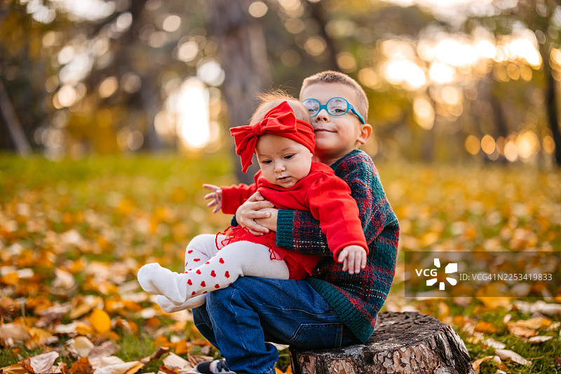 秋日，学龄前男孩在公园里举起他的小妹妹图片素材