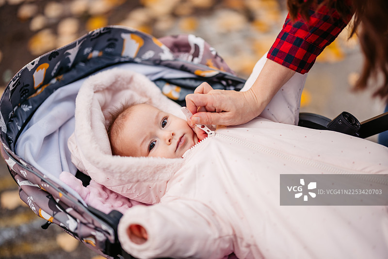 年轻的母亲在公园的婴儿车里给她的女儿穿上外套图片素材