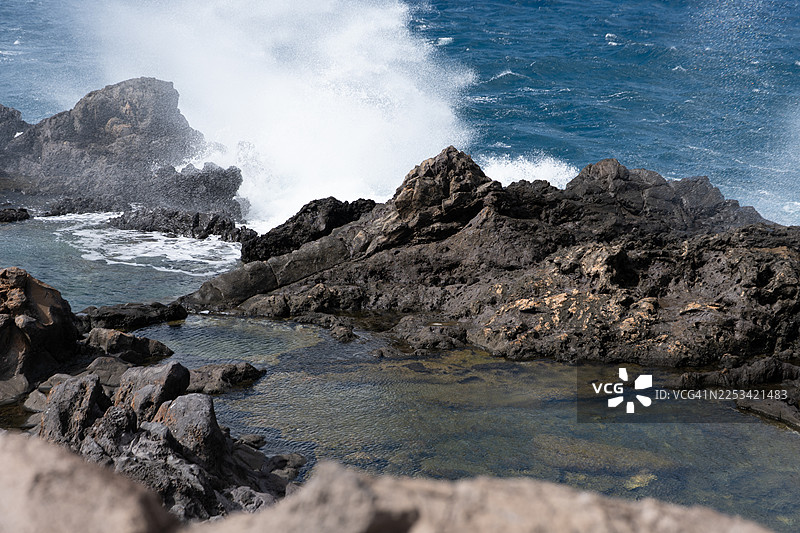 阳光灿烂的日子里，强大的海浪拍打着崎岖的火山岩，形成了戏剧性的海岸景象，美国卡帕鲁瓦图片素材
