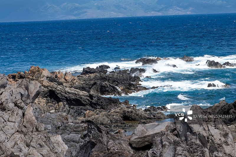 阳光明媚的日子里，戏剧性的海浪拍打着崎岖的火山岩石，展现出大自然的原始力量，美国卡帕鲁瓦图片素材