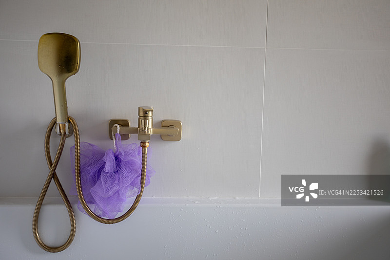 干净浴室里现代金色淋浴喷头和水龙头特写，旁边有一个紫色的沐浴海绵图片素材