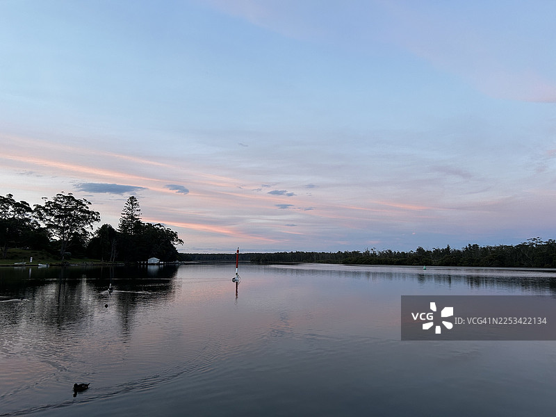 宁静的湖景，柔和的粉彩日落色调倒映在水中，四周环绕着茂密的树木，澳大利亚苏塞克斯湾图片素材