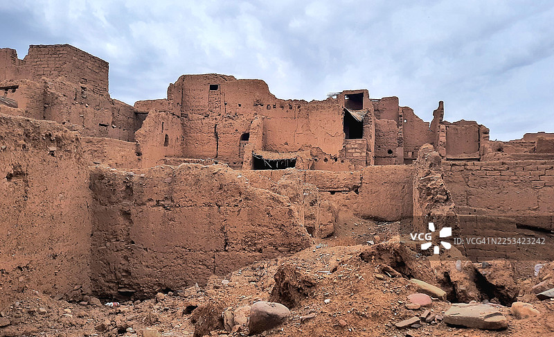 仰视角度拍摄的古老泥砖遗址，背景是多云的天空，展现了历史建筑和破败景象，地点：阿格迪兹，摩洛哥图片素材