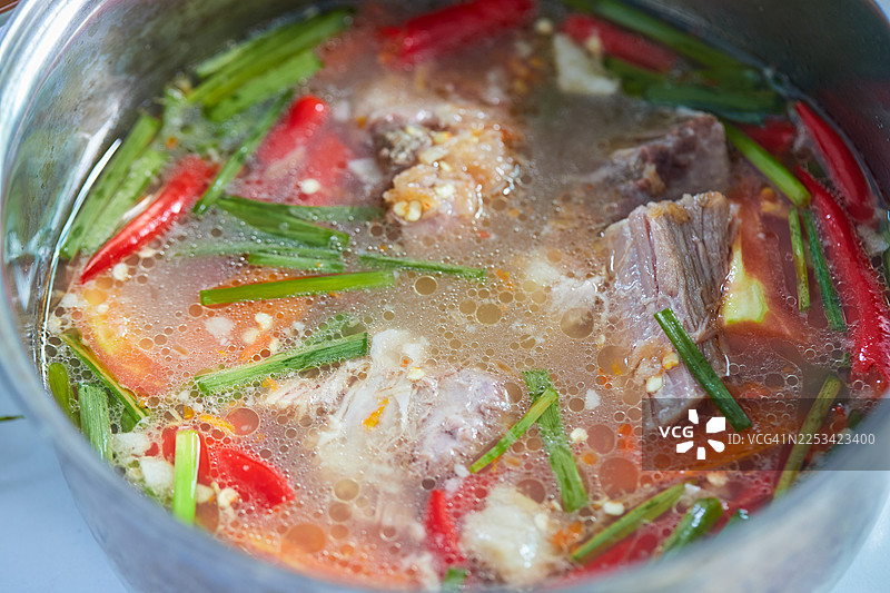 炖煮浓郁肉汤的特写，配有肉类、红辣椒和绿色香草，展现出浓郁而美味的汤底图片素材