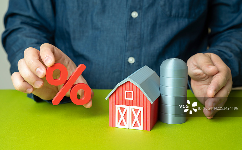 男人之手，带有百分比符号和一个模型农场，代表农业贷款或利率图片素材