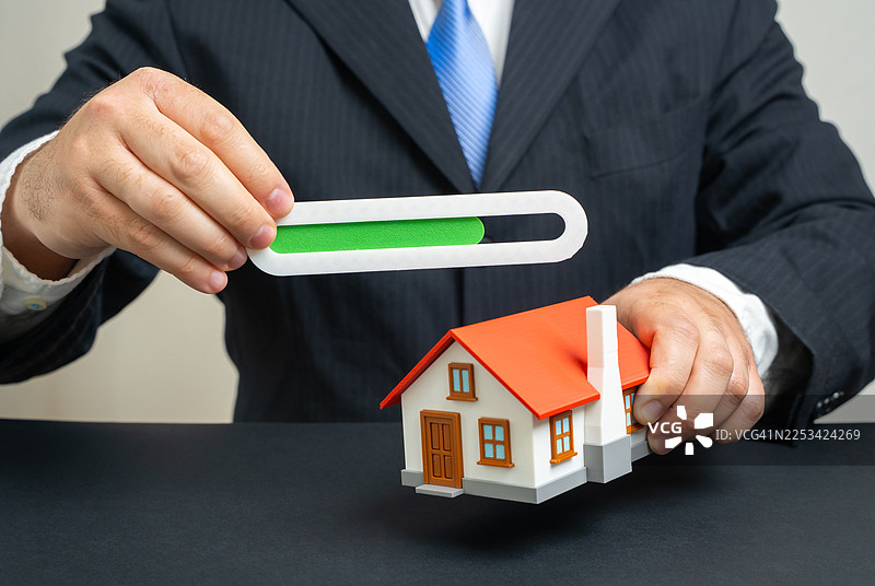 商人手持房屋模型和进度条，象征房地产开发或投资进展图片素材