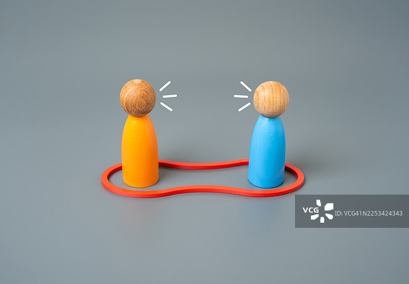 两个木制玩具人偶被一条红线连接，象征着沟通与连接图片素材