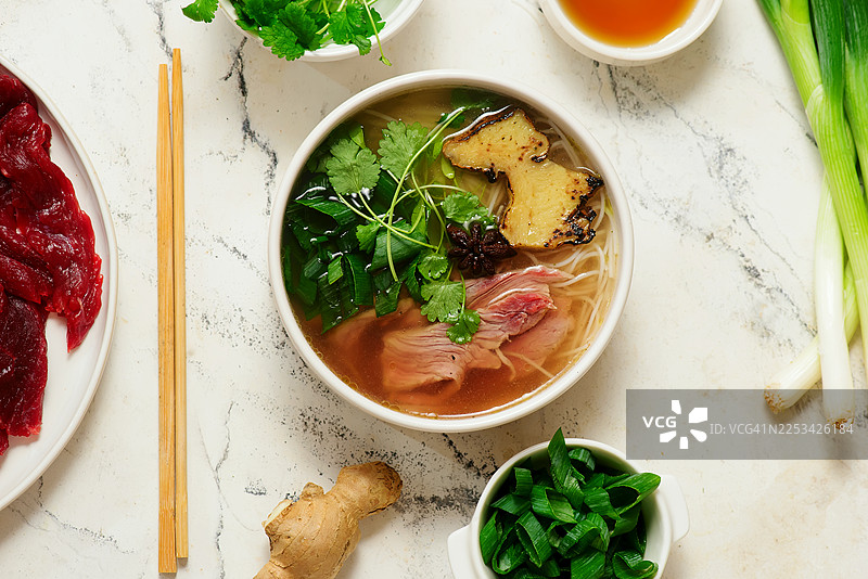 大理石桌面上盛放着一碗越南河粉，配有新鲜食材的俯视镜头图片素材