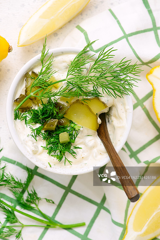 俯视视角，格子桌布上放着一碗奶油莳萝酱，配有腌黄瓜和柠檬图片素材