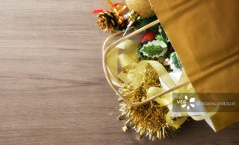 俯视角度拍摄的圣诞装饰品和礼物从纸袋中散落在木桌上，留有复制空间图片素材