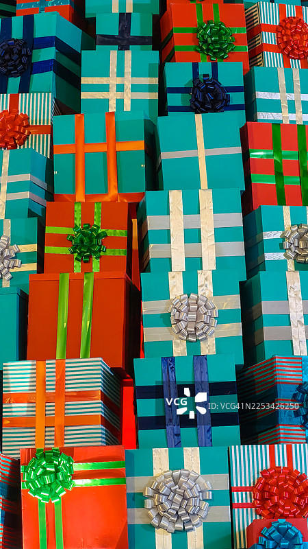 俯视角度拍摄的彩色包装礼品盒堆叠在一起，包装盒包括红色、青色和蓝色，并带有丝带，背景充满节日气氛。图片素材