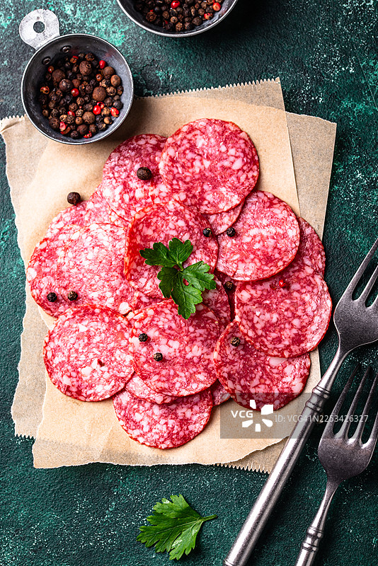 俯视拍摄的美味萨拉米香肠片，撒有胡椒粒和欧芹，置于乡村风格的深绿色背景上图片素材