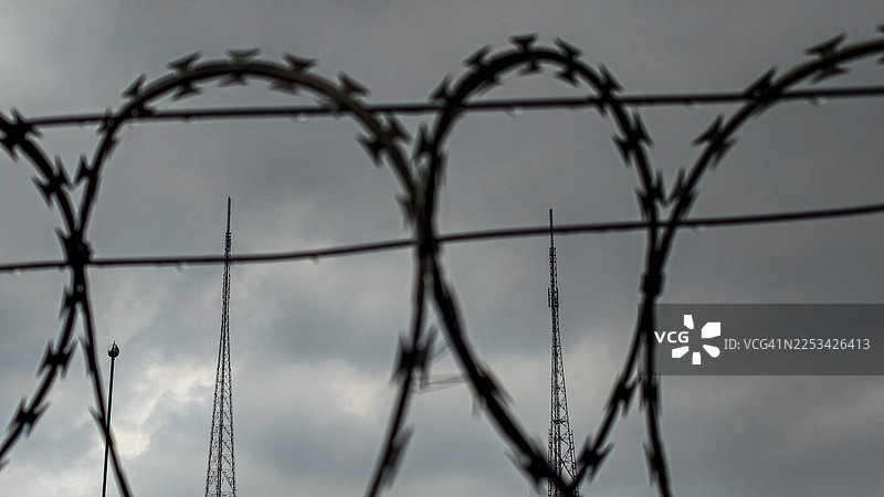 阴沉天空下的带刺铁丝网围栏与电信塔图片素材