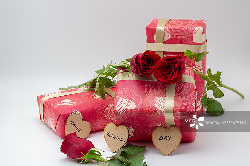 情人节礼盒，用带有心形图案的红纸包装，装饰有红玫瑰和心形标签，背景为纯色图片素材