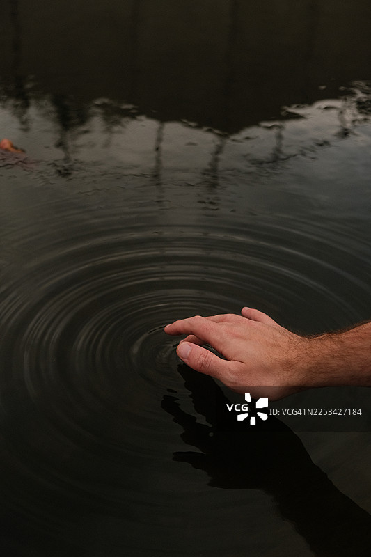 男人手部特写，触碰黑暗的水面，泛起涟漪图片素材