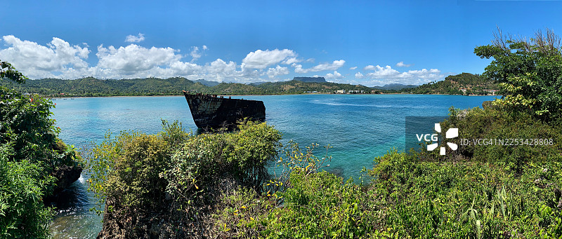 热带海湾的全景，有古老的沉船、郁郁葱葱的绿色山丘和清澈的蓝天图片素材