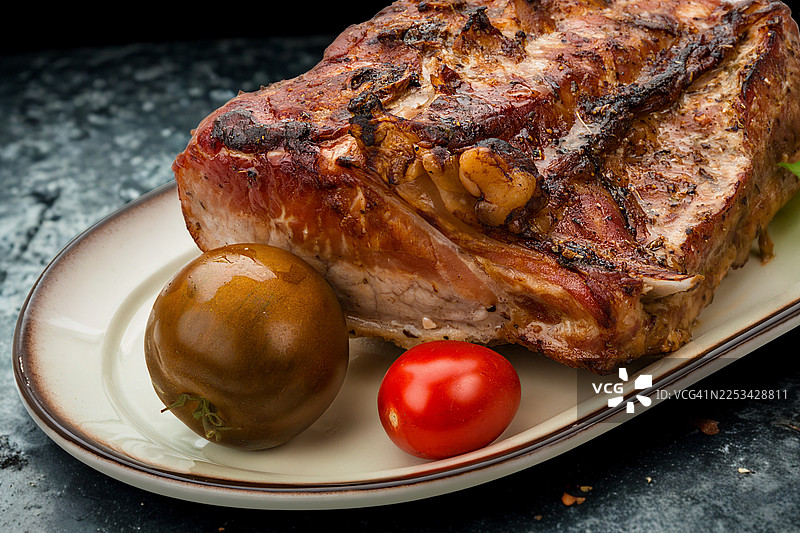 盘子里放着几块烤得恰到好处、调味均匀的猪肋排，配上新鲜的番茄，已准备好上桌。图片素材