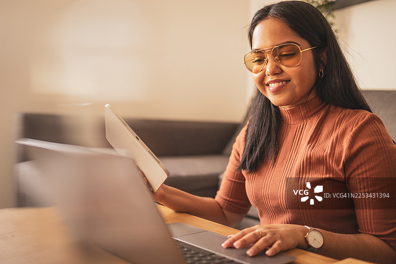 戴眼镜的女性在家中使用笔记本电脑和平板电脑工作图片素材