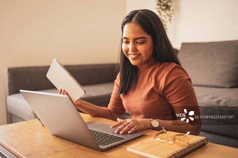 年轻女子在现代家居中一边使用平板电脑一边用笔记本电脑工作图片素材