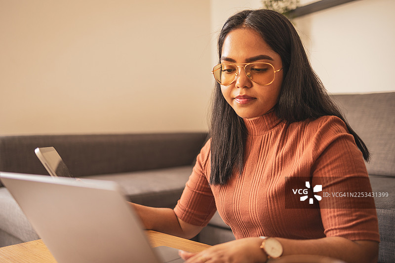 一位女士在舒适的家中，使用笔记本电脑和平板电脑工作图片素材