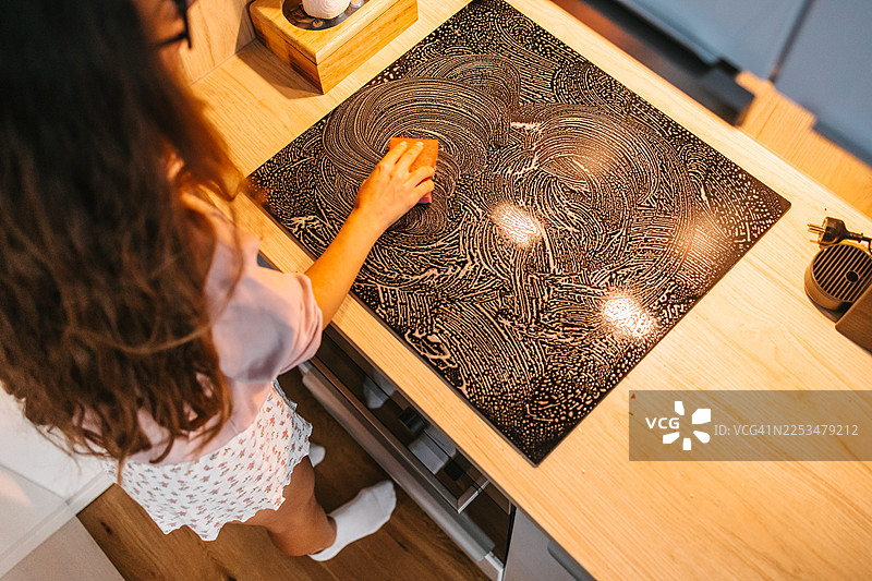 女人在现代厨房里用海绵清洁玻璃陶瓷炉灶图片素材