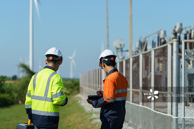 工程师正在检查一座大型风力发电机的运行情况，该发电机正在风电场中工作以发电。（照片）图片素材
