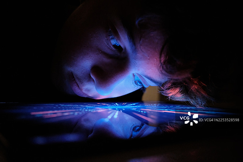 年轻人使用发光的数字屏幕，屏幕光倒映在桌子上图片素材