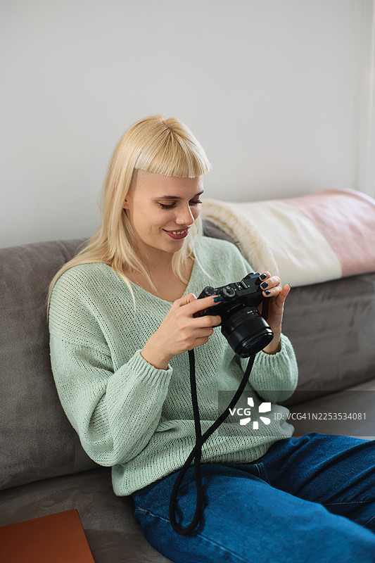 一位年轻的时尚女性正舒适地躺在沙发上，查看相机里的照片。图片素材