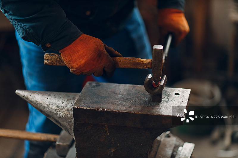 铁匠在工作室的铁砧上用锤子敲打炽热的金属图片素材