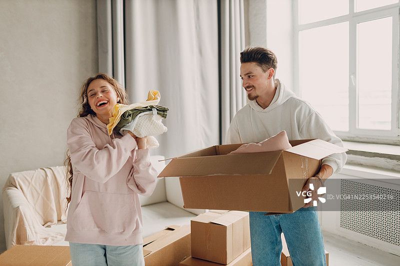 一对幸福的情侣在新家拆箱整理物品，周围堆满了纸箱。图片素材