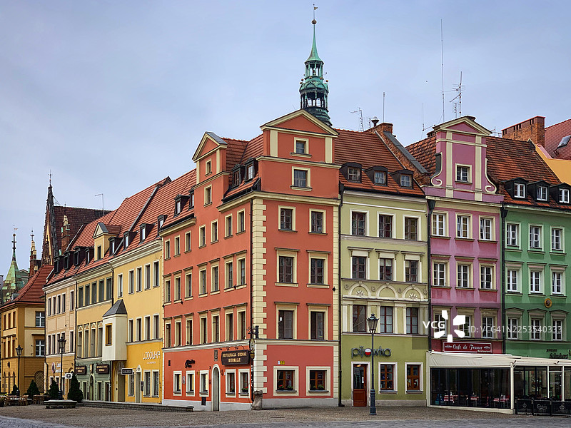 明亮的蓝天下，一排色彩缤纷、外墙精美的历史建筑沿鹅卵石街道排列，波兰图片素材