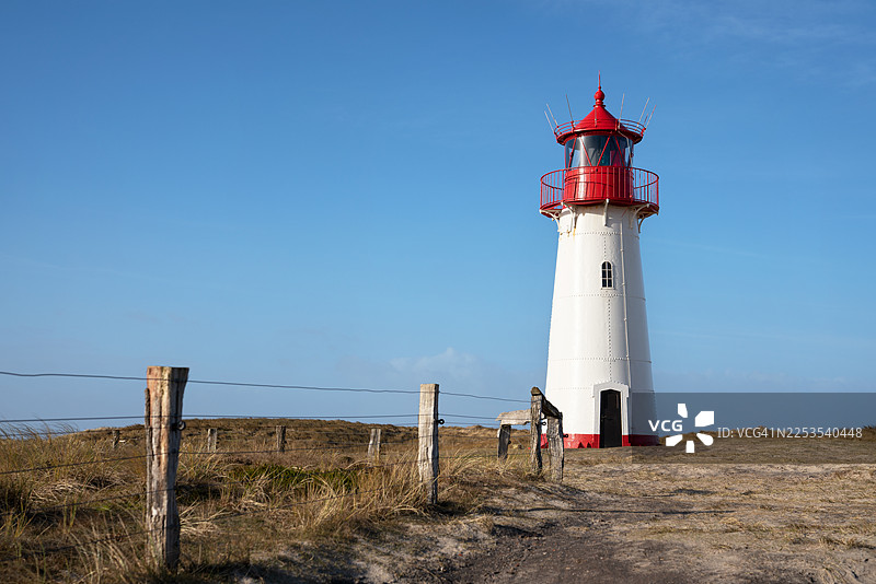 德国坎彭标志性的红顶灯塔，坐落于长满青草的沙丘上，背景是湛蓝的天空图片素材